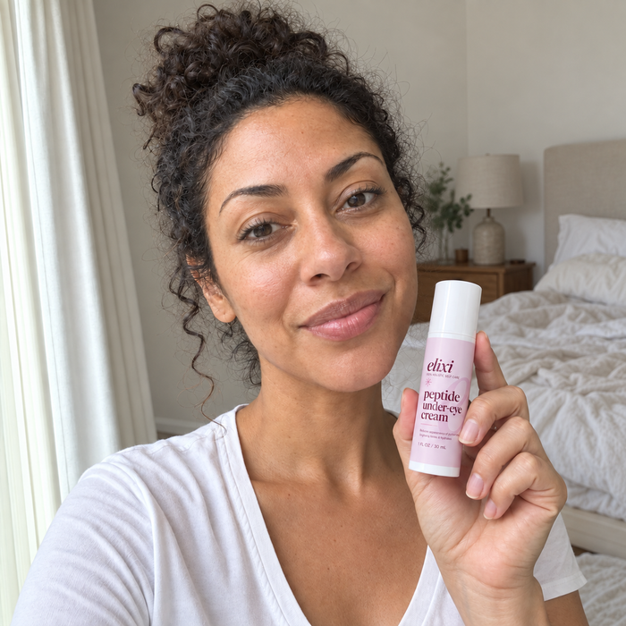 Woman with curly hair holding Elixi Peptide Under-Eye Cream in a bedroom