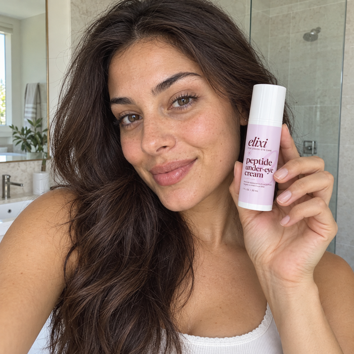 Woman with long dark hair holding Elixi Peptide Under-Eye Cream in a bathroom