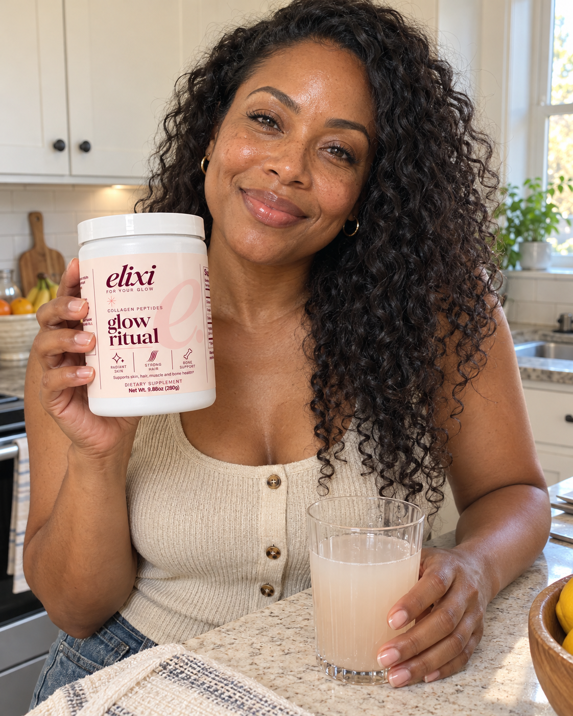 Woman holding Elixi Glow Ritual collagen peptides at a kitchen counter with a glass