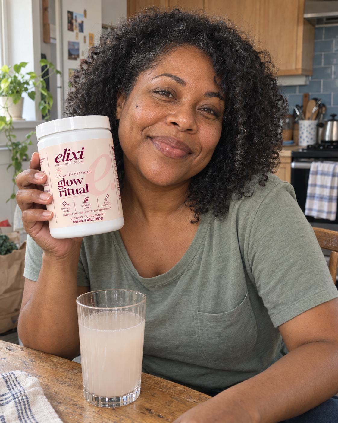 Woman holding Glow Ritual beside a glass in her kitchen